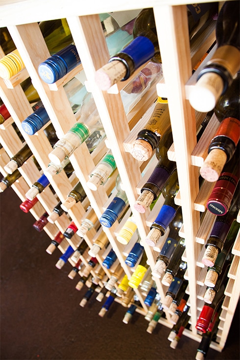 A close-up photograph of many wine bottles on a wooden rack in a restaurant.