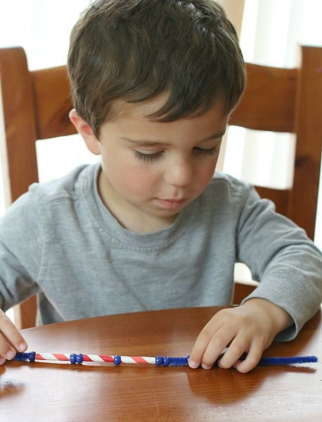 little boy sitting down on wooden chair holding Patriotic Necklace on the table