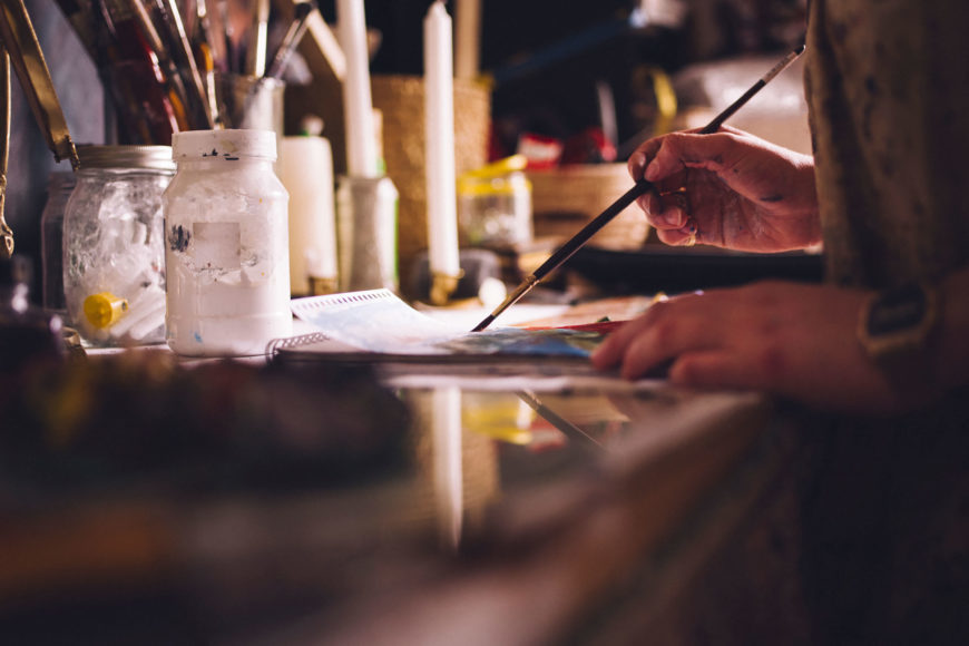 Person doing acrylic painting with painting materials on the table