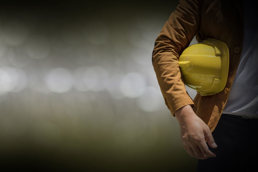 Crop image of a man standing on the right side with hard hat on his shoulder