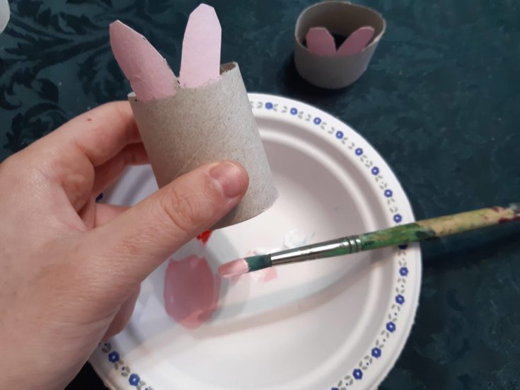 Hand holding a cardboard tube with cut out bunny features paind in pink.