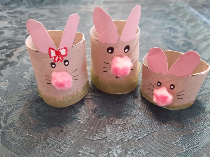 Three cardboard tube bunnies with pink pompom noses and added grass features below.