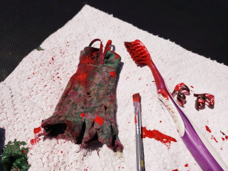 Dirty cloth and shoes of barbie doll splattered with red paint on a tissue paper.
