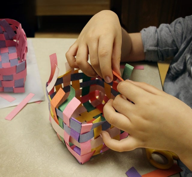 Arts and crafts with the hands of a child crafting a basket made of construction paper as a symbol of art education at schools or other creative activities for kids.