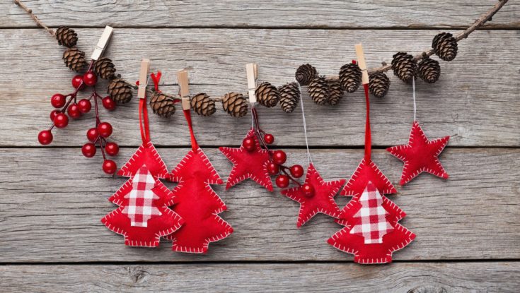 Christmas and New Year decorations made of felt are hanging on stick with pinecones, rustic wooden background, copy space