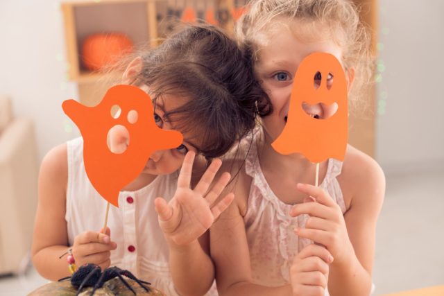 Little girls hiding faces behind paper ghosts