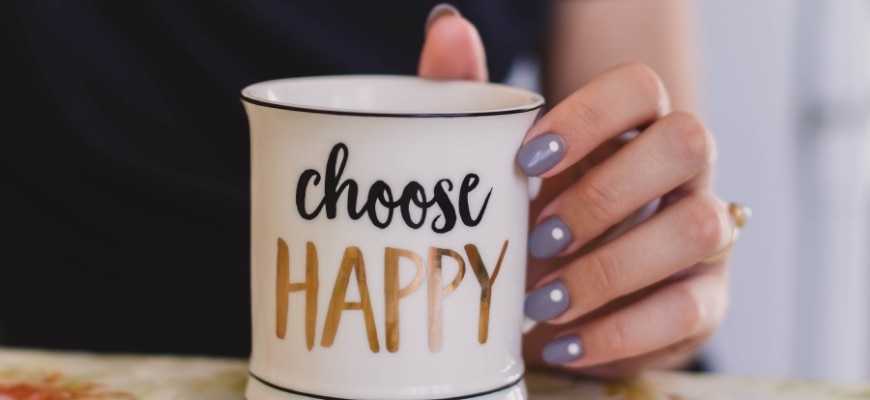 Woman's hand holding mug with a printed word "Choose Happy"