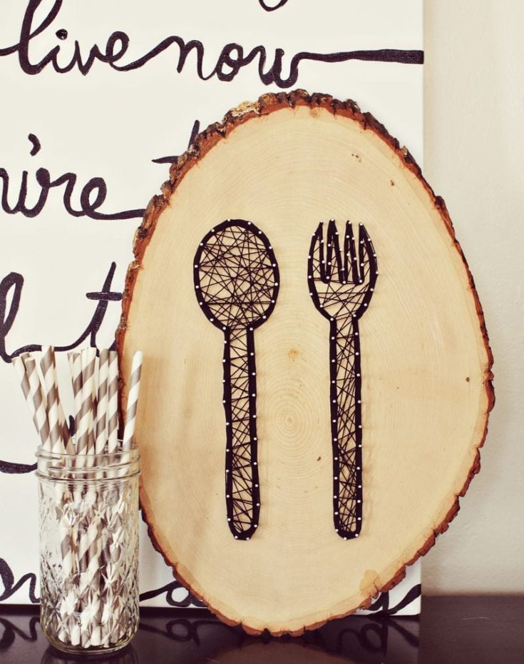 String art cutlery design on round wood plank.