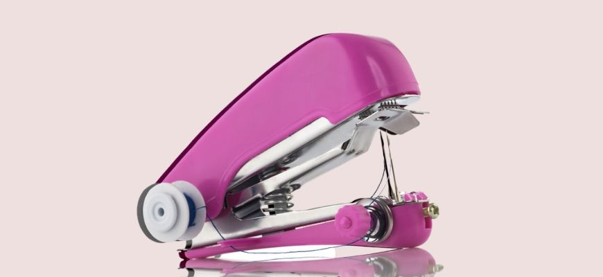 Pink mini handheld sewing machine isolated on light pink background
