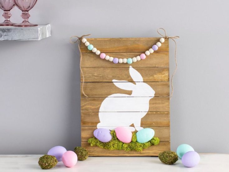 A DIY painted wooden sign, painted with white rabbit and colorful easter eggs using clay and plastic moss green.