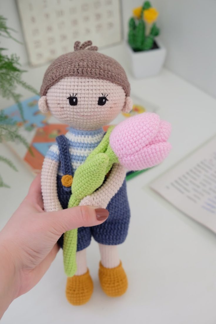 Close up shot of woman's hand holding a crocheted doll with bouquet of crocheted tulips.