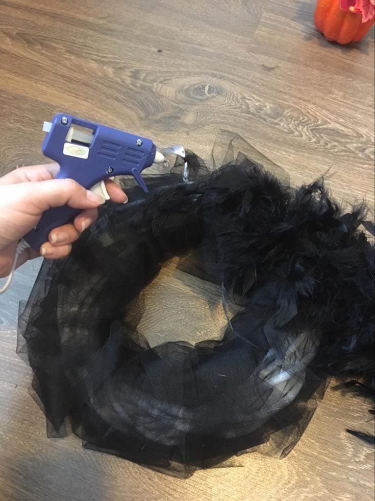 a hand holding a glue gun putting a glue on wreath to stick some black feathers on it