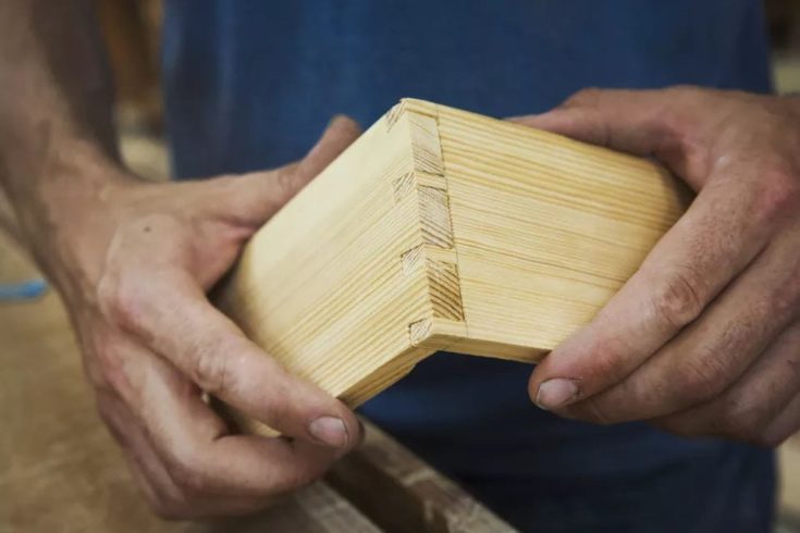 Close up of person working a boat builders workshop joining together two pieces of wood.