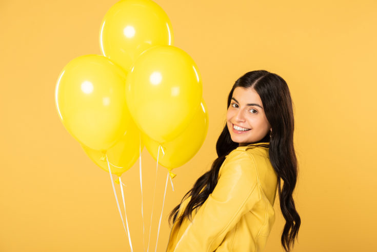 Brunette happy woman holding yellow balloons, isolated on yellow