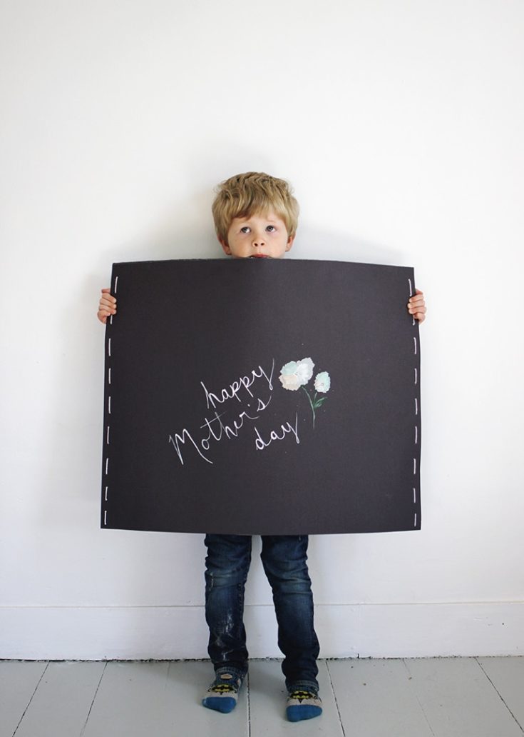 A boy holding an illustration board with a written greetings for mother's day.