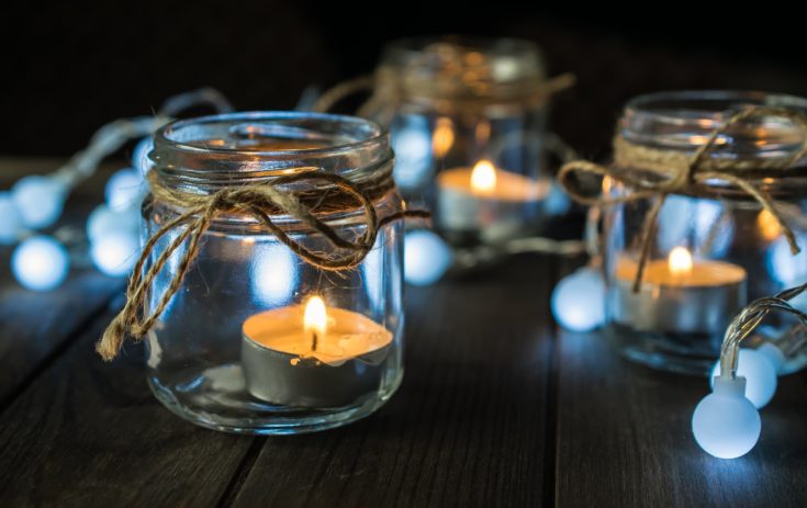 Decorative dark and moody composition with mason jar candles and lights on wooden table