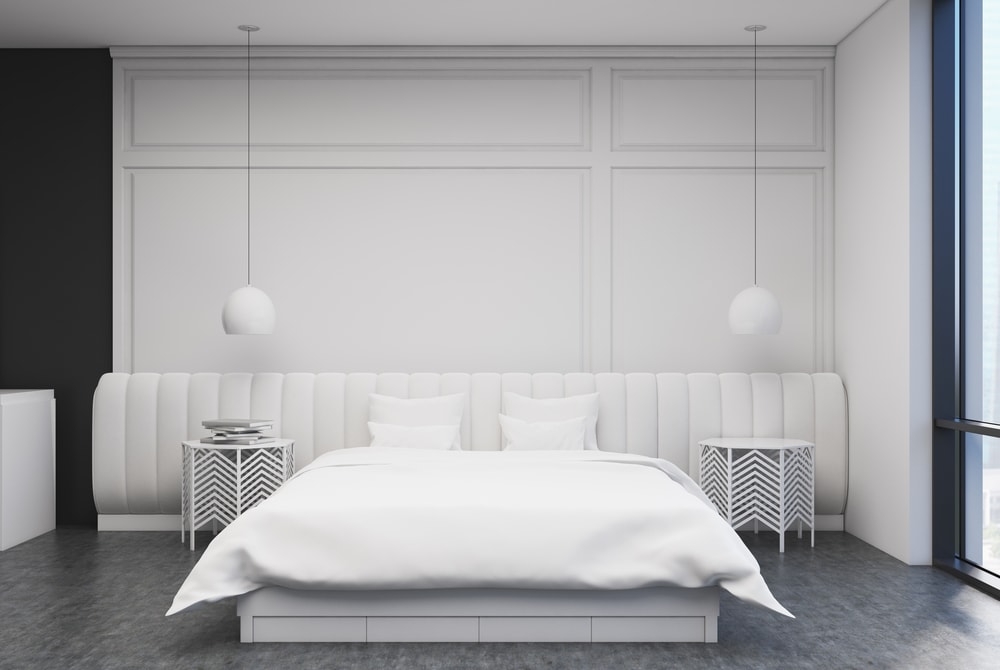 White bedroom interior with a concrete floor, a large bed with a white cover and two bedside tables. 3d rendering mock up