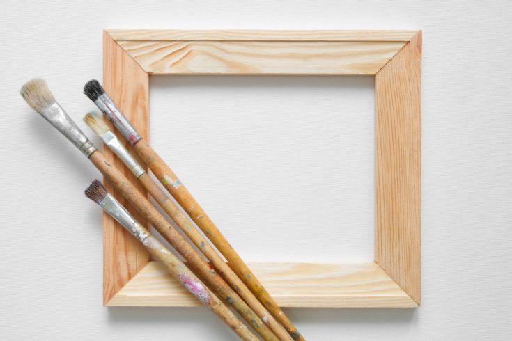 Wooden stretcher bar and paintbrushes on white artist canvas background. Top view. Copy space for text.