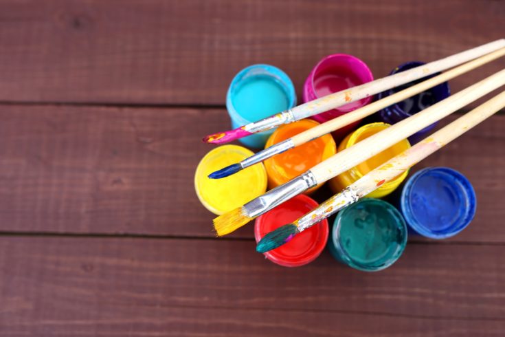 Colorful acrylic paints with paint brushes on wooden background