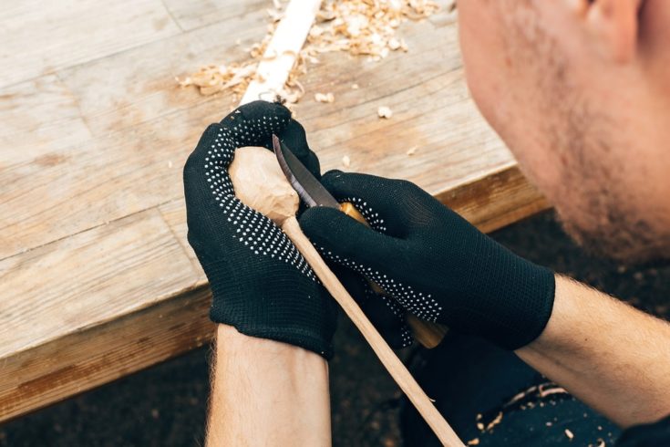 Hands carving spoon from wood, working with chisel close up. Process of making wooden spoon, chisel and shavings on dirty table. Wooden workshop. Handmade festival in summer park