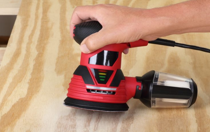 Electric circular sander sanding a piece of plywood