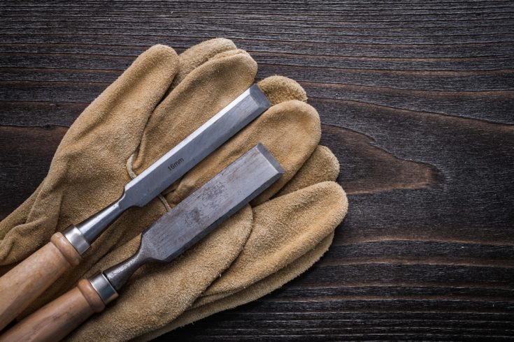 Pair of brown leather gloves with firmer chisels on vintage wooden board construction concept.