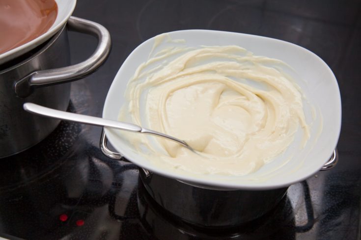 White chocolate couverture in a water bath on a stove with spoon.