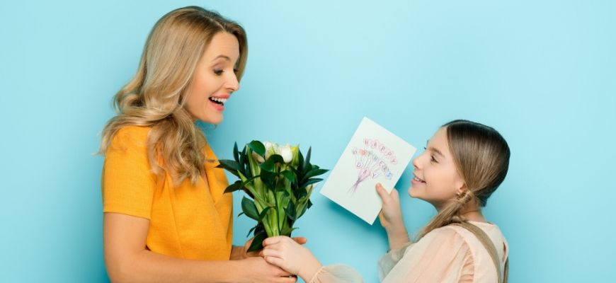 Daughter give her mother a flower bouquet and greeting card.