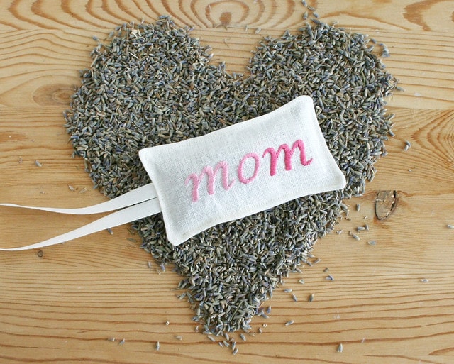 Embroidered lavender sachets for Mom on top of lavender seeds in arrange in a heart shape.