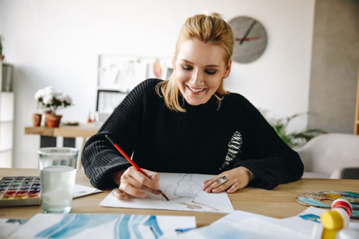 A smiling fashion designer drawing sketch with a glass of water in the table