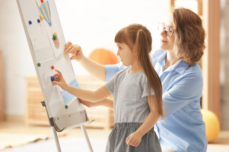 Female psychologist with cute little girl during art therapy