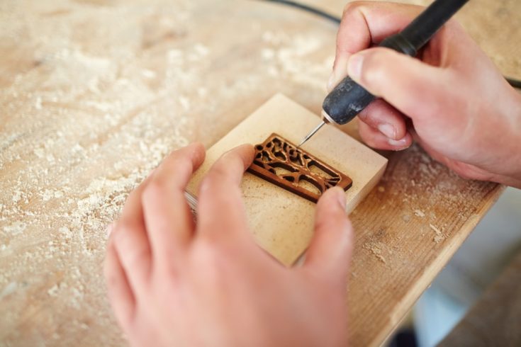 Hands of master of burning ornaments carving wooden board with pyrographic equipment