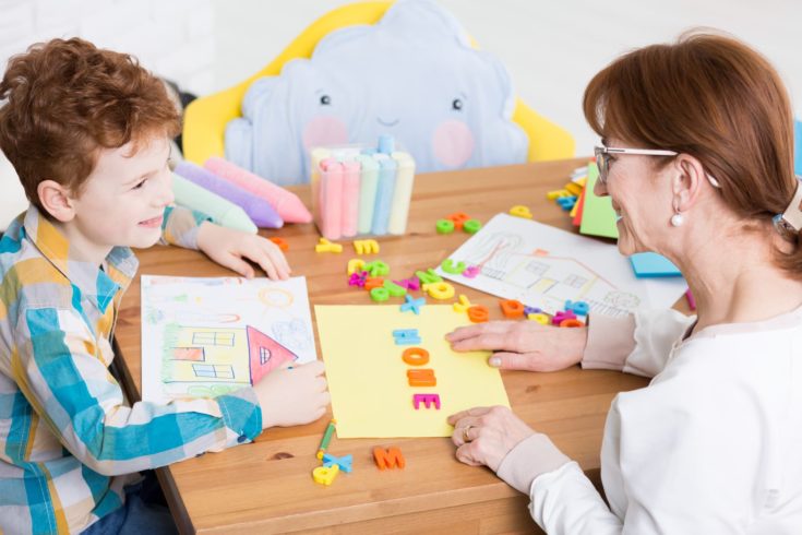 Happy little boy having speech problem. Speech therapist helping her patient to read