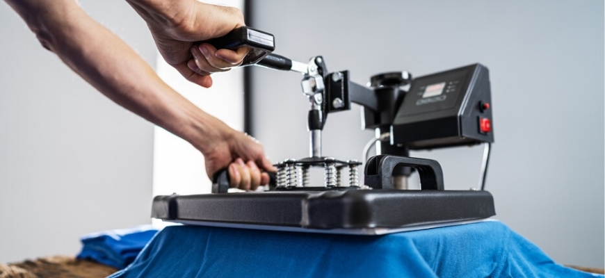 Close up shot of hands holding a heat press,applying pressure on a blue t-shirt