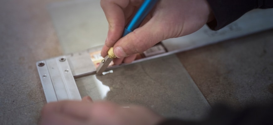 Focus shot on man's hand holding a glass cutter and the other hand holding the steel T- ruler.