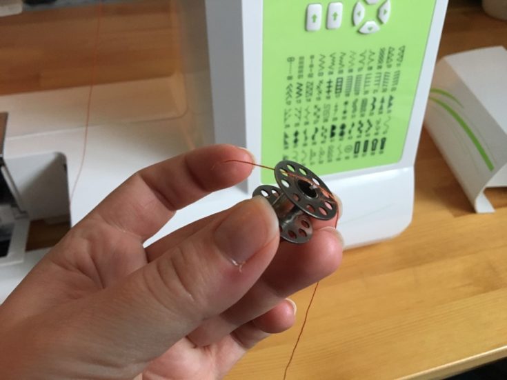 a close up shot of a person's hand holding the bobbin and a thread