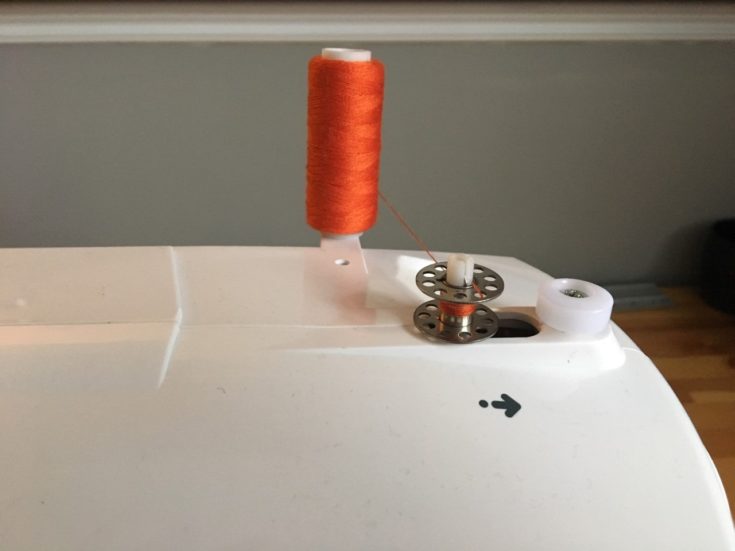 orange thread inserted into the one hole of the bobbin