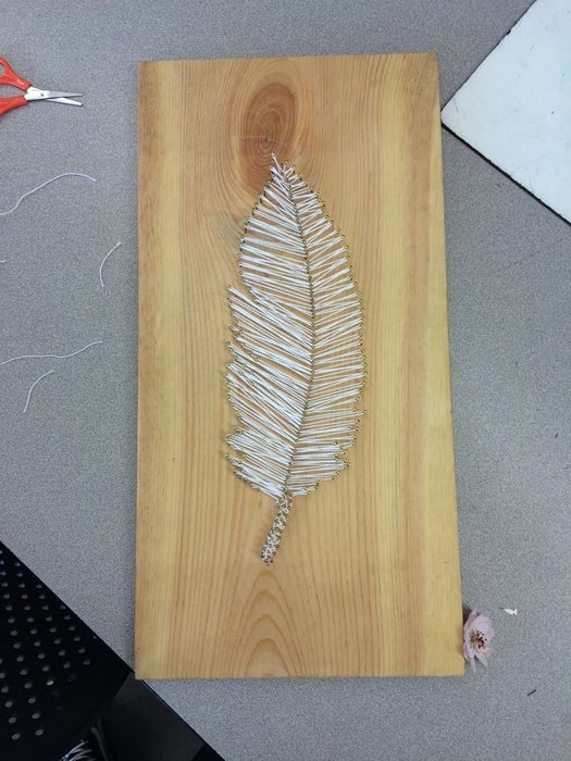 Leaf string art design on a wooden plank.