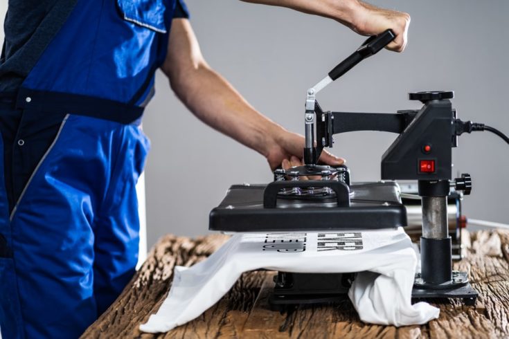 Man Printing On a white T Shirt In Workshop using heat press machine