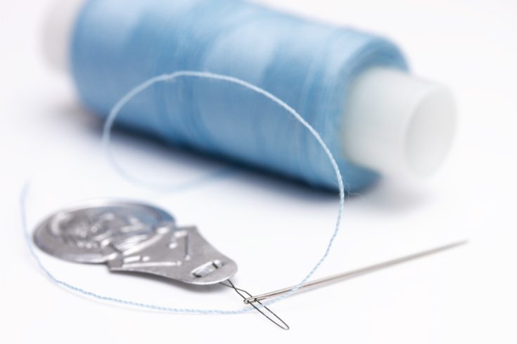 Needle threader, needle and spool of thread on white background