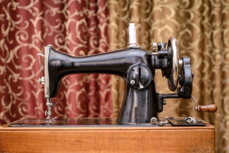 Old black sewing machine white spool of thread on the background of blinds