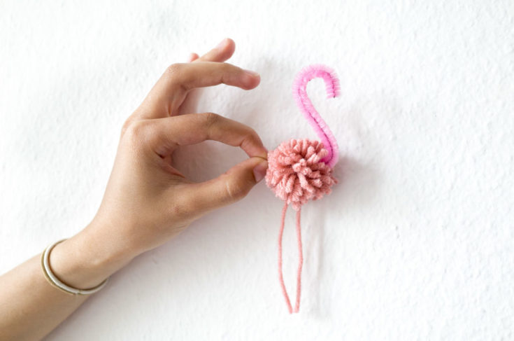 a hand holding a Pom Pom Flamingos on a white wall