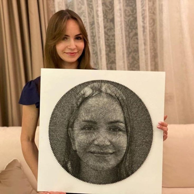 Young woman holding her portrait made by a string art.