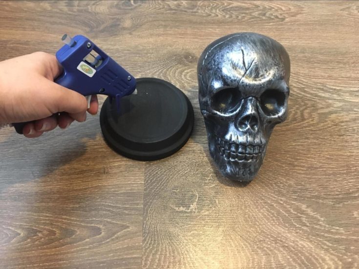 Putting glue on terra cotta saucer using a glue gun with plastic skull on the side