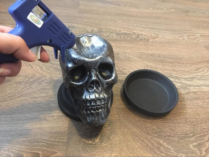a hand holding a glue gun, pointing to the top of the plastic skull