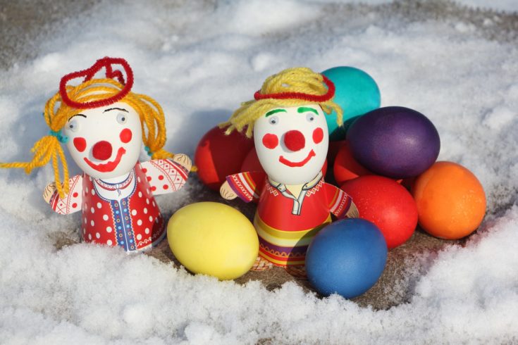 Color Easter eggs with a toy figure of the little man on a napkin in snow outdoors