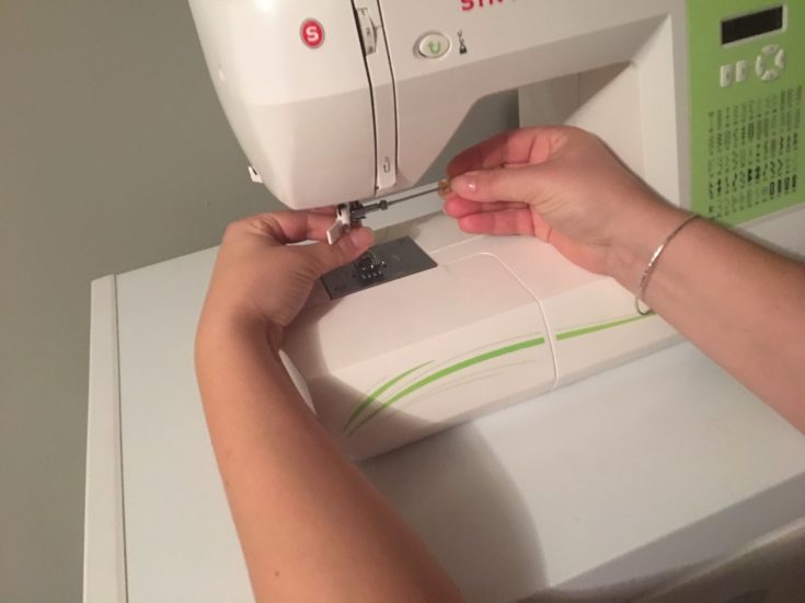 a shot of a person's hand tightening a screw on the needle of sewing machine