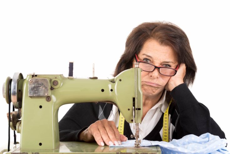 Stressed senior woman with sewing machine isolated in white