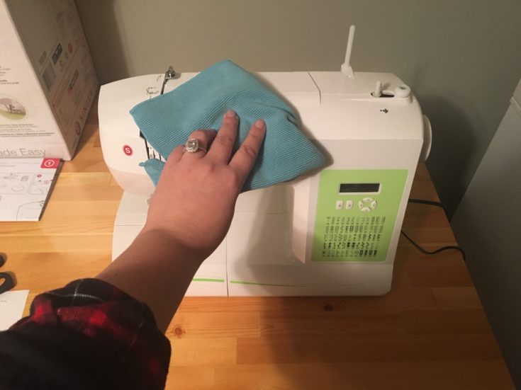 a woman's hand cleaning the external case of the sewing machine using a cleaning cloth