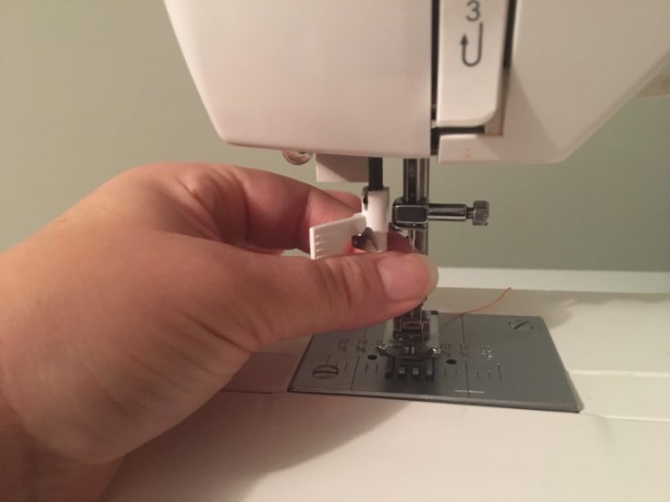 a close up shot of a person's hand inserting a new needle to the sewing machine